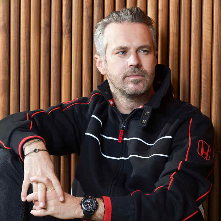 Homem de chapéu e casaco Honda Racing, a tocar na aba do chapéu.