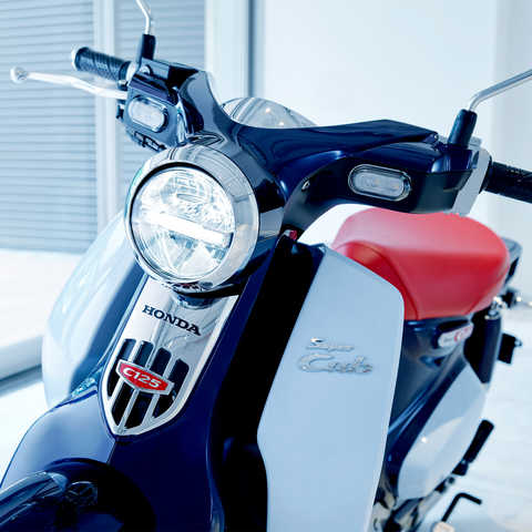 Honda Super Cub estacionada num cen&aacute;rio moderno.