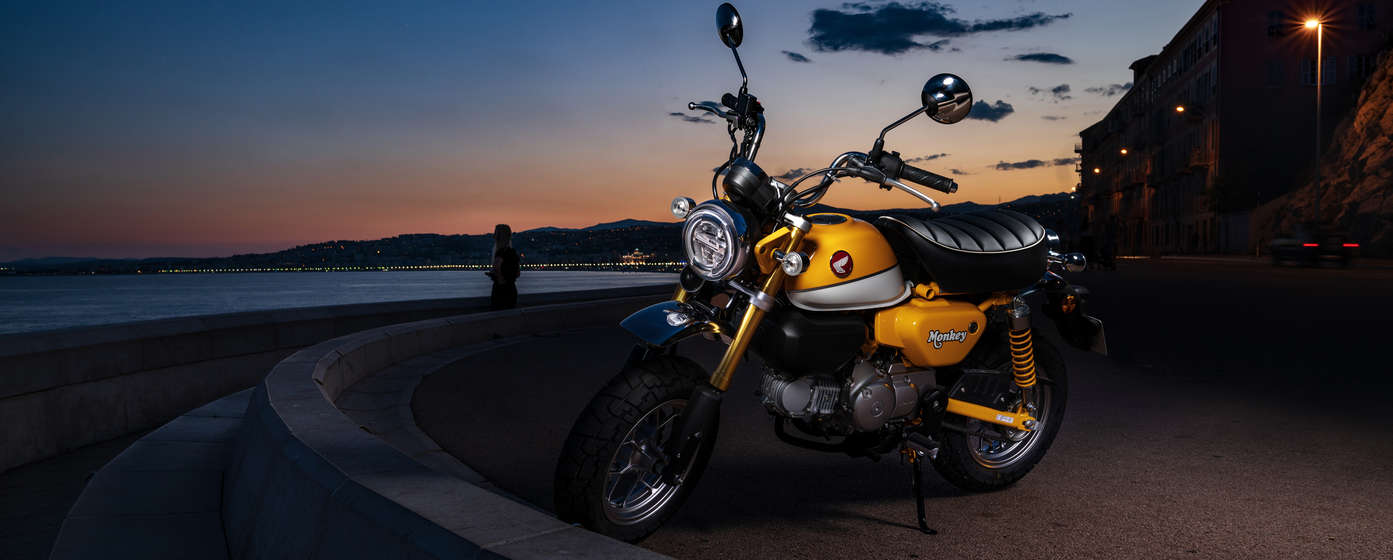 Honda Monkey estacionada em frente à praia.