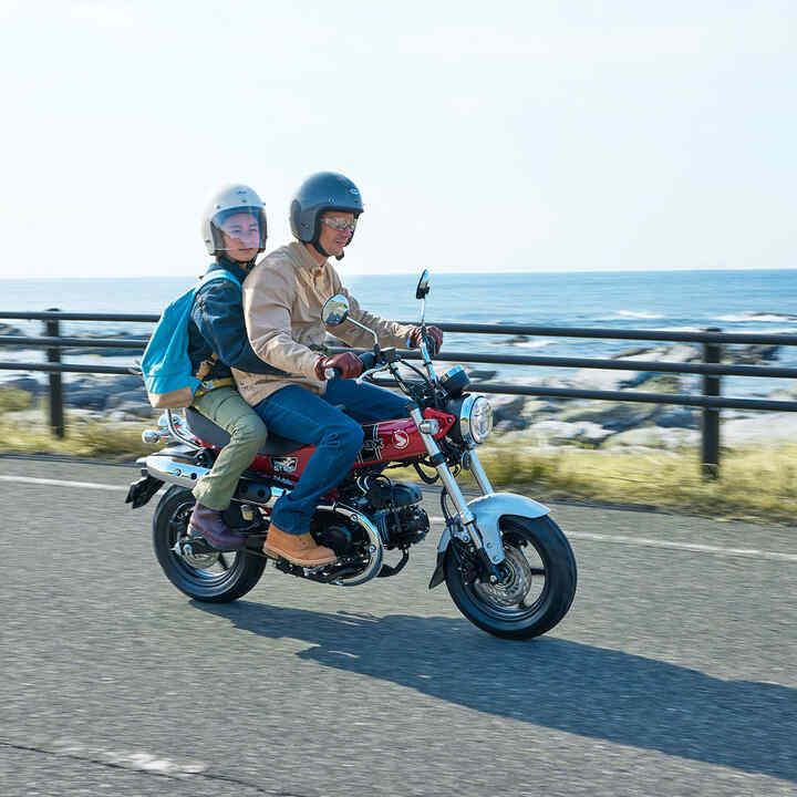 Honda Dax 125 em estrada costeira com condutor e passageiro