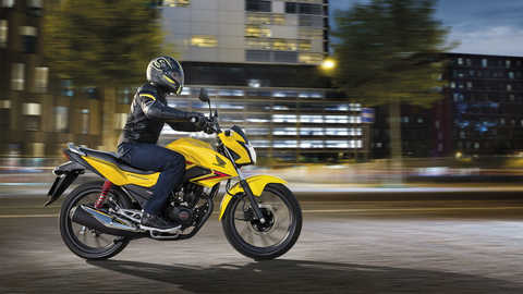 Vista lateral de uma CB125F em amarelo Pearl Twinkle, virada para a direita, em estrada (localiza&ccedil;&atilde;o urbana)