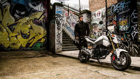 Honda MSX125 estacionada numa &aacute;rea urbana com o condutor junto &agrave; moto