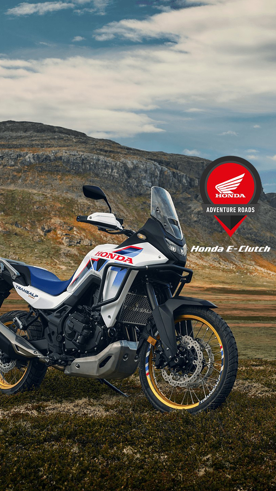 A Honda adventure motorcycle, likely the Honda E-Clutch model, parked on rugged terrain with mountains in the background. The bike is white with red and blue accents. The Honda logo and \"ADVENTURE ROADS\" text are visible in the top right corner of the image.