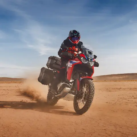 Condutor a bordo de uma Honda CRF1100 Africa Twin Adventure Sport num cenário de deserto.