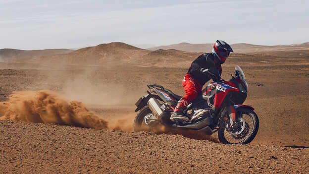 Modelo a conduzir uma mota CRF1100L Africa Twin num cenário de deserto.