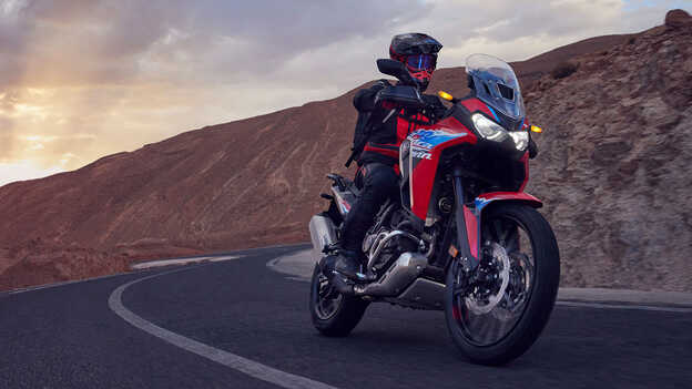 Modelo a conduzir uma mota CRF1100L Africa Twin num cenário de deserto.