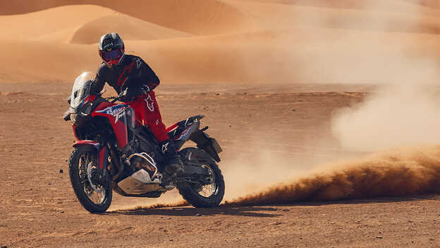 Modelo a conduzir uma mota CRF1100L Africa Twin num cenário de deserto.