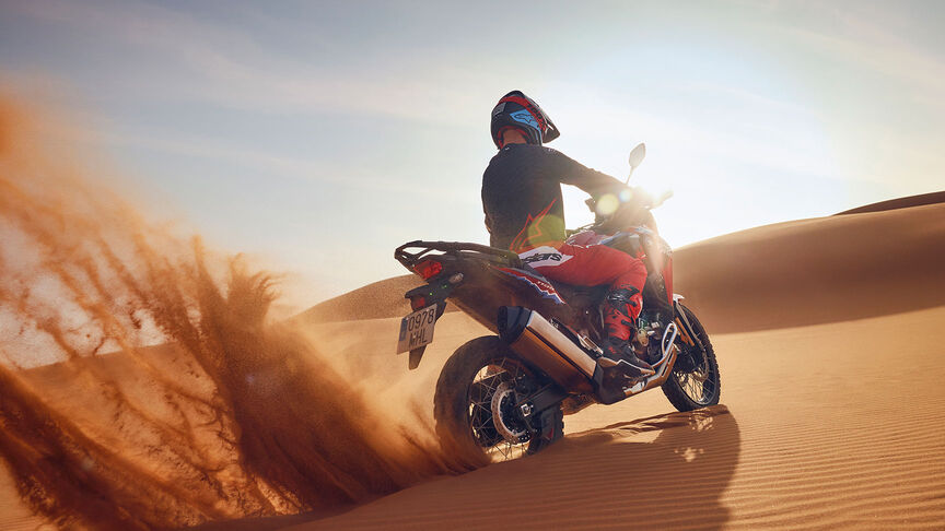 Modelo a conduzir uma mota CRF1100L Africa Twin num cenário de deserto.