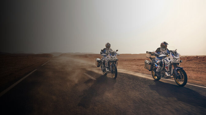 Vista frontal a 3/4 de ocupantes na CRF1100 Africa Twin Adventure Sports na estrada no deserto. 
