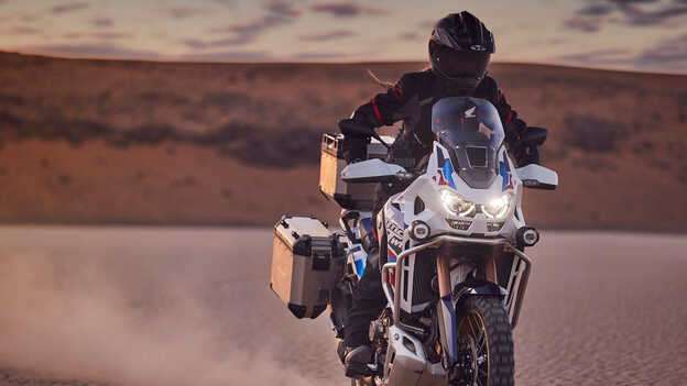 Condutor a bordo de uma Honda CRF1100 Africa Twin Adventure Sports num cenário de deserto.