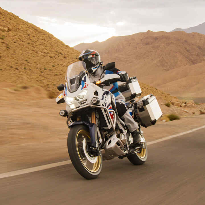 Condutor a bordo de uma Honda CRF1100 Africa Twin Adventure Sports num cenário de deserto.