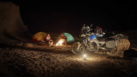 Duas pessoas a acampar e vista lateral da Honda Africa Twin Adventure Sports estacionada &agrave; noite.