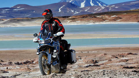 Vista dianteira de tr&ecirc;s quartos da Honda Africa Twin Adventure Sports com condutor, cen&aacute;rio de montanha.