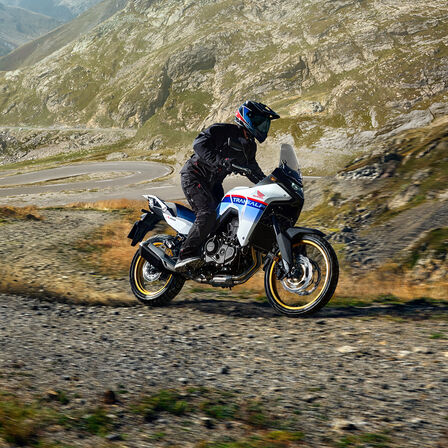 XL750 Transalp num trilho de gravilha à frente de montanhas.