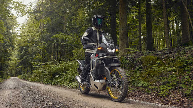 Modelo a conduzir uma Honda XL750 Transalp num local florestal.
