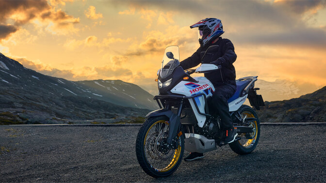 Modelo a conduzir uma moto XL750 Transalp na estrada em local de montanha.