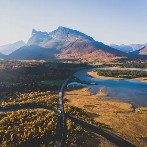 Paisagem montanhosa escandinava clássica no verão com estrada, montanhas e um fiorde sob um céu azul, norte da Noruega, condado de Finnmark, filmado a partir de um drone