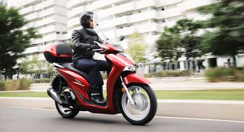 Honda SH125i, vista lateral direita dianteira a 3 quartos, com condutor, na cidade
