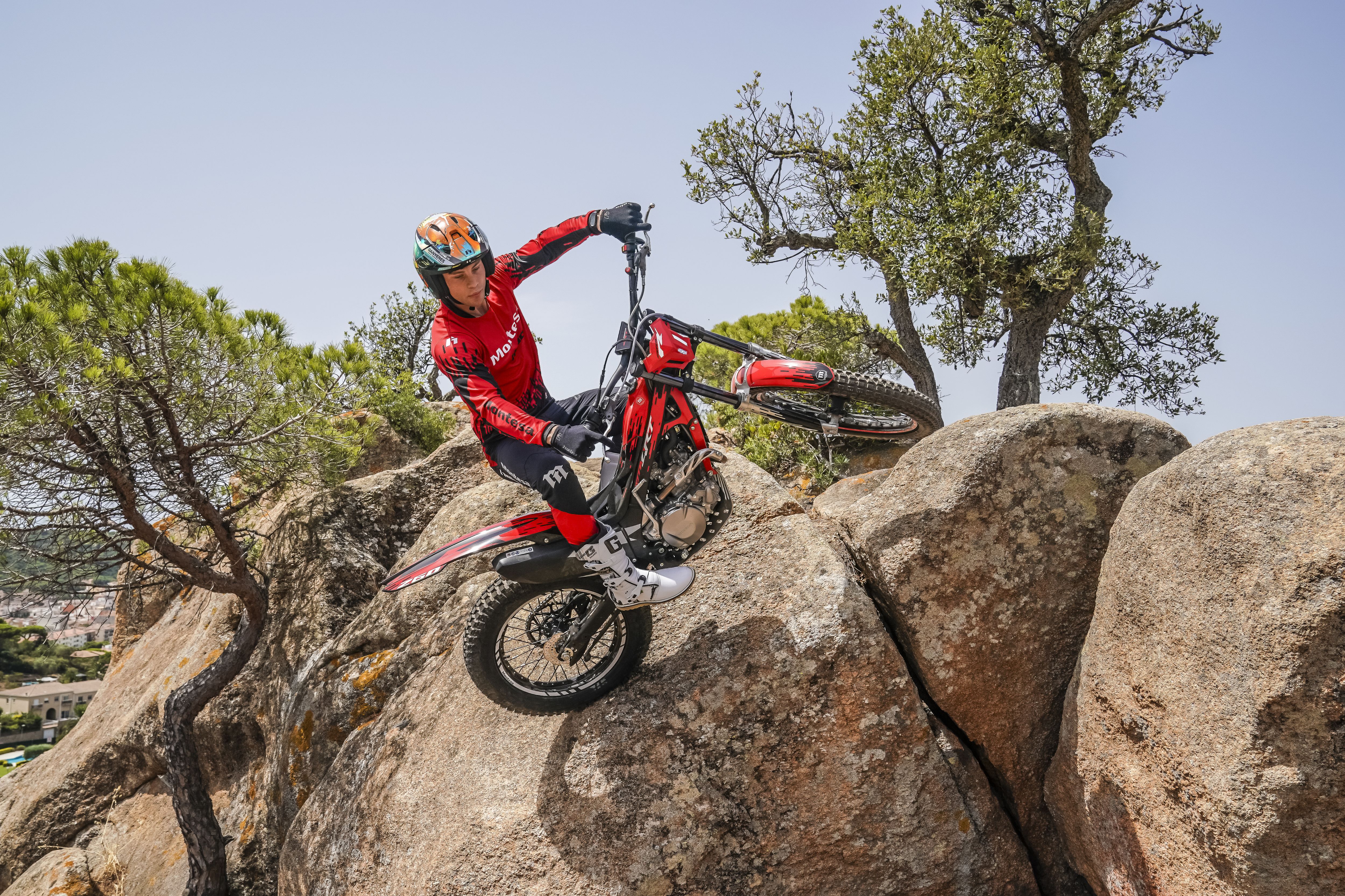Motociclista a manobrar uma Montesa Cota 4RT 260R vermelha sobre rochas íngremes num dia soalheiro.