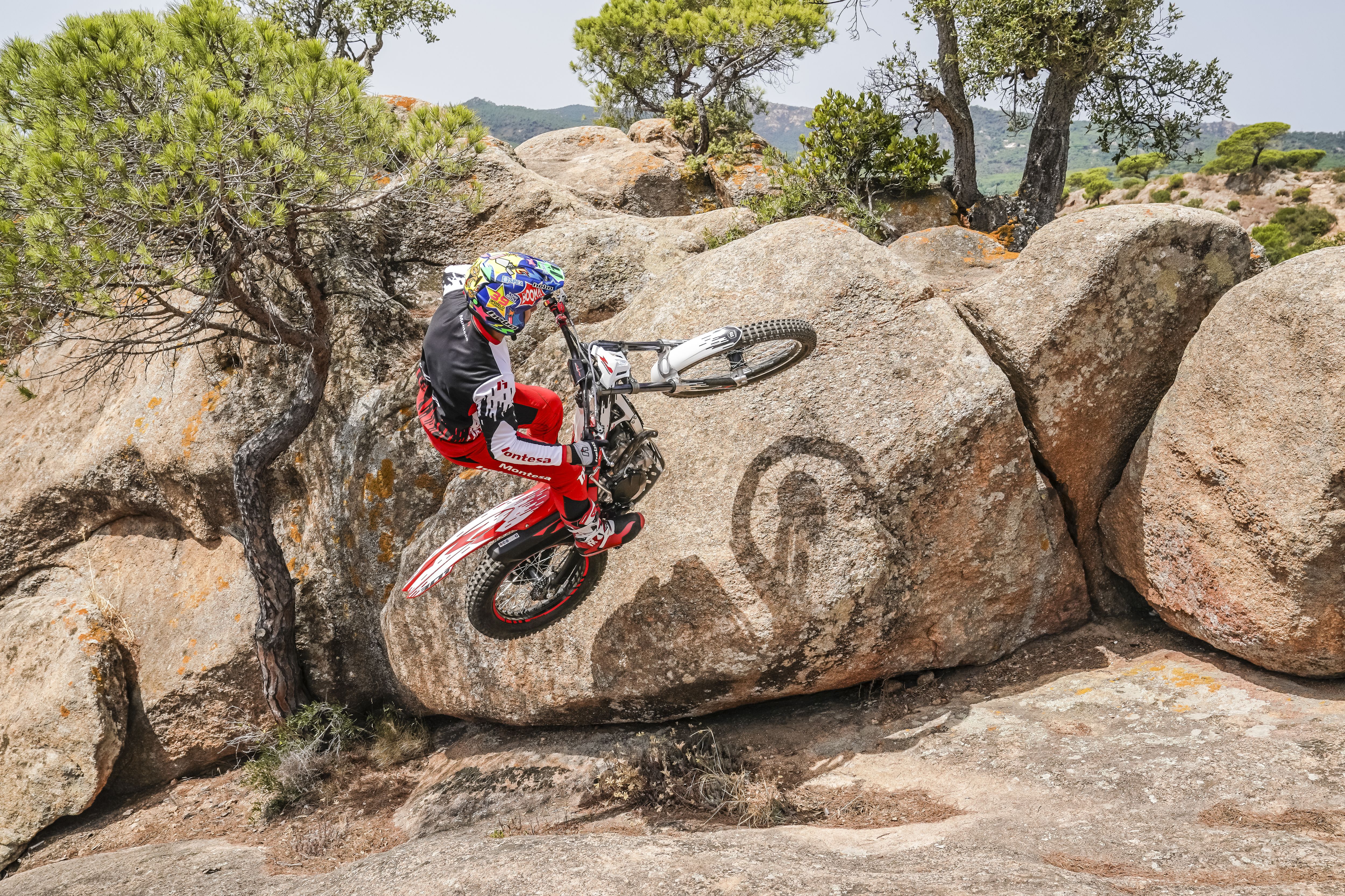 Motociclista a fazer um cavalinho numa Montesa Cota 301RR sobre uma formação rochosa.