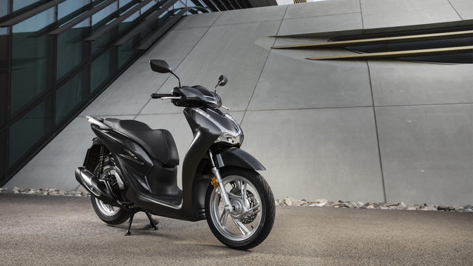 Honda Sh125i com mala traseira e para-brisas numa rua.