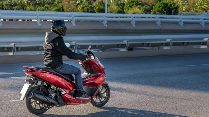 Vista lateral da Honda PCX125 com condutor numa localização urbana.