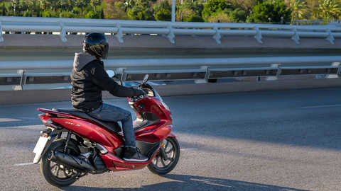 Vista lateral da Honda PCX125 com condutor numa localiza&ccedil;&atilde;o urbana.
