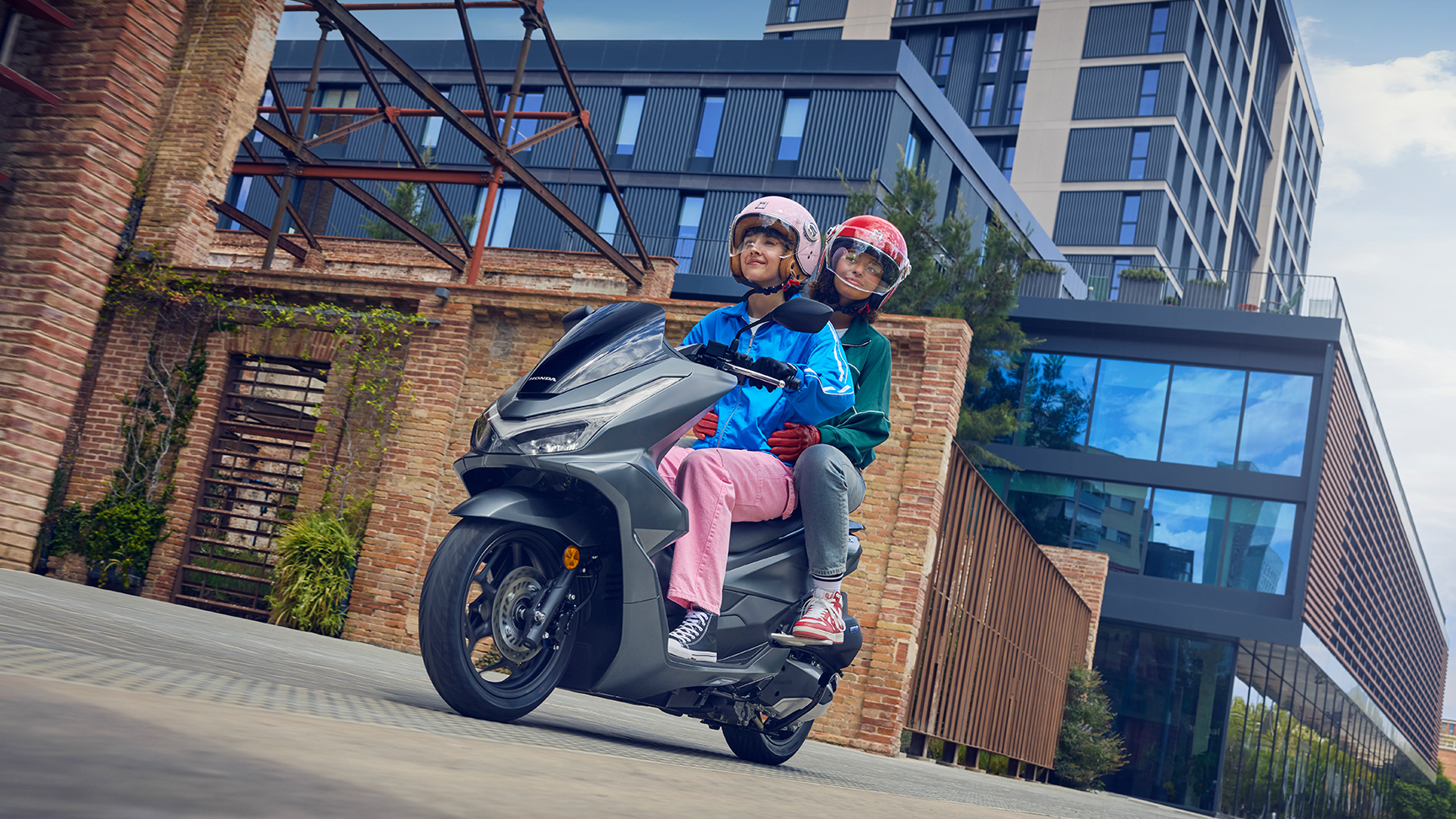 Models riding a PCX125 motorcycle in a city location.