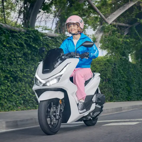 Modelo a conduzir uma moto PCX125 num cenário urbano.