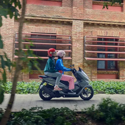 Fotografia lateral de modelos a conduzir a moto PCX125 num cenário urbano.