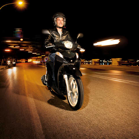 Perspetiva dianteira a três quartos da scooter Honda SH Mode preta com condutor. Virada para a direita (em estrada).