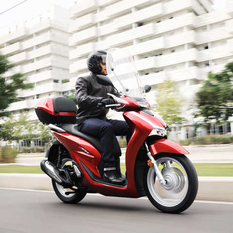Honda-SH125i vista lateral direita dianteira a 3 quartos, com condutor na cidade