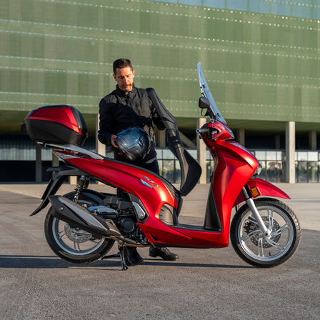 Honda SH350i, homem de pé junto à scooter, vista traseira, moto vermelha