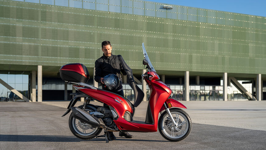 Honda SH350i, vista a 3 quartos dianteira direita, com condutor, na estrada, moto vermelha