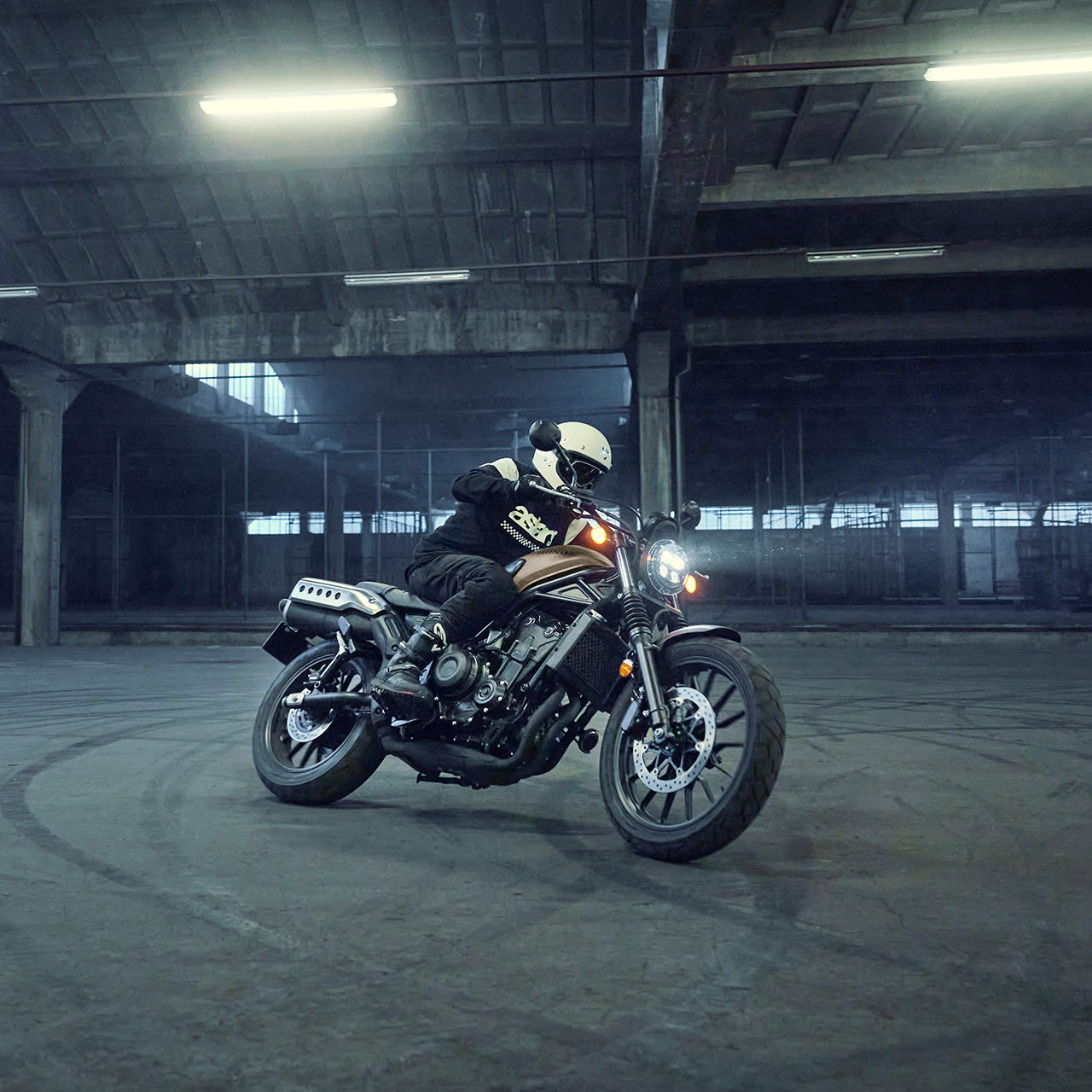 Modelo a conduzir a moto Honda CL500 num cenário de estacionamento.