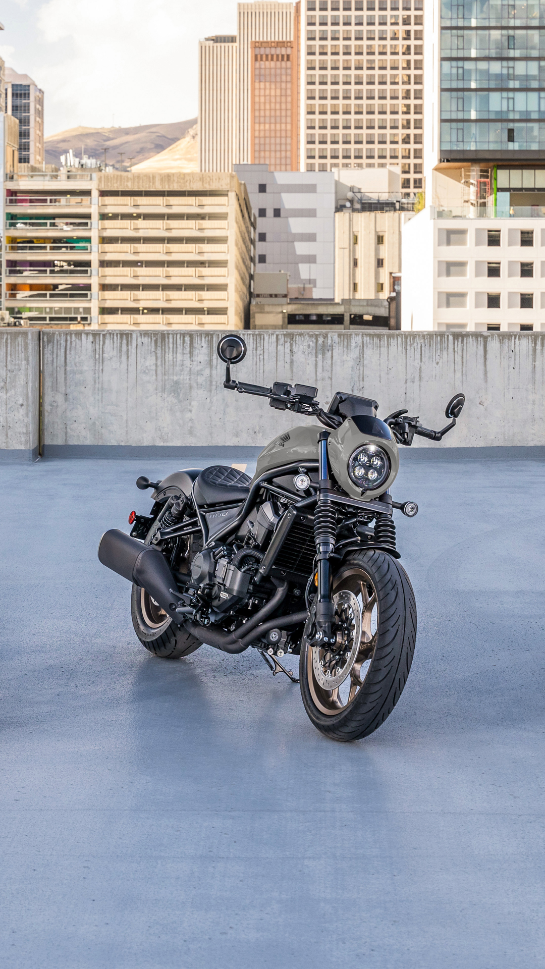 Uma moto CMX1100 no exterior, à frente de um edifício moderno.