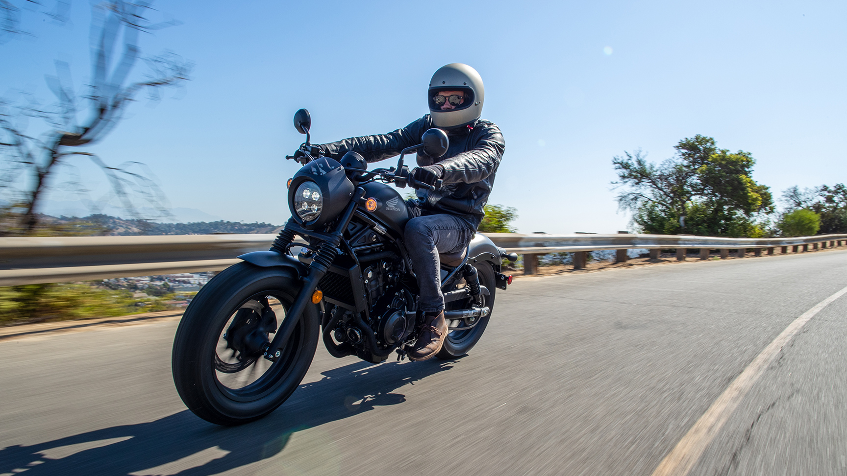 Condutor sobre uma Honda CMX500 Rebel numa cenário de estrada.