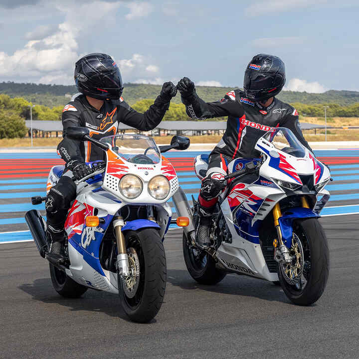 Dois condutores sentados em Honda Fireblades de frente batendo punhos na pista de corridas.