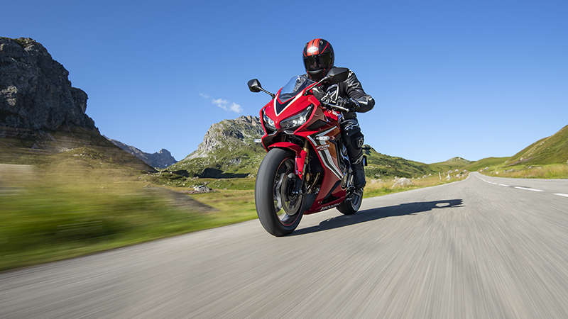 CBR650R, vista frontal lateral esquerda a 3 quartos, com um condutor em movimento numa estrada de montanha